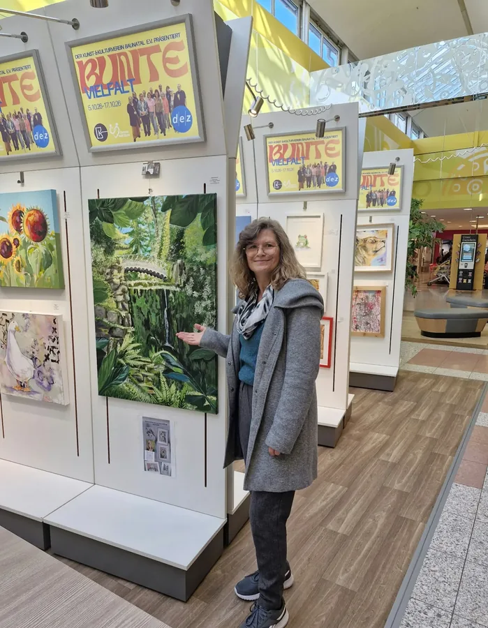 Brigitte Weinhold zeigt in der Ausstellung im dez auf ihr Bild mit Brücke und Wasserfall